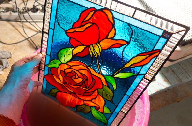 May include: A stained glass panel featuring two red roses with green leaves on a blue background. The panel is framed with a silver border.
