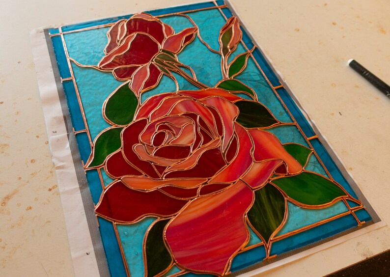 May include: A stained glass window panel featuring a red rose with green leaves on a turquoise background.