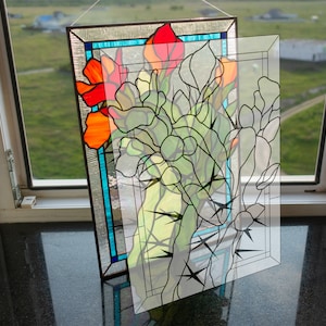 Puede incluir: Un panel de vitral con un diseño floral con flores rojas, naranjas y verdes. El panel está enmarcado en negro y tiene una capa protectora transparente sobre el vidrio.