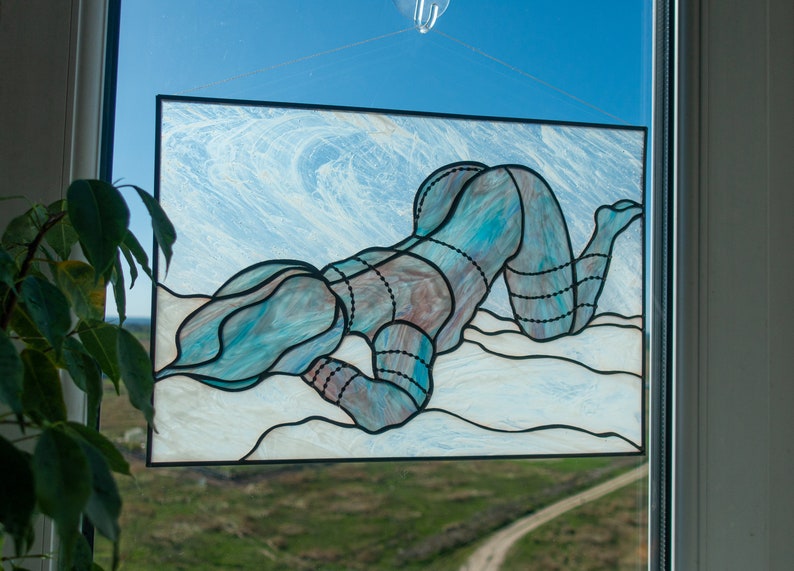 May include: A stained glass window depicting a person in a blue and white patterned suit lying on their stomach. The background is a white and blue swirl pattern.