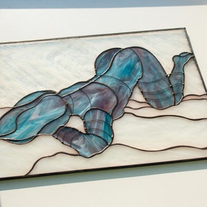 May include: A stained glass artwork depicting a figure in a blue and purple pose, lying on a white background with a wavy pattern.