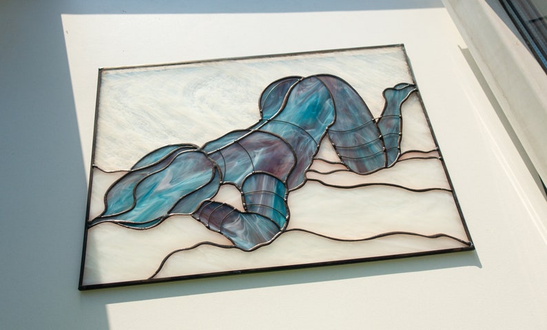 May include: A stained glass artwork depicting a figure in a blue and purple pose, lying on a white background with a wavy pattern.