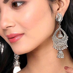 May include: Silver tone dangle earrings with a peacock design, a bell charm, and a beaded fringe.