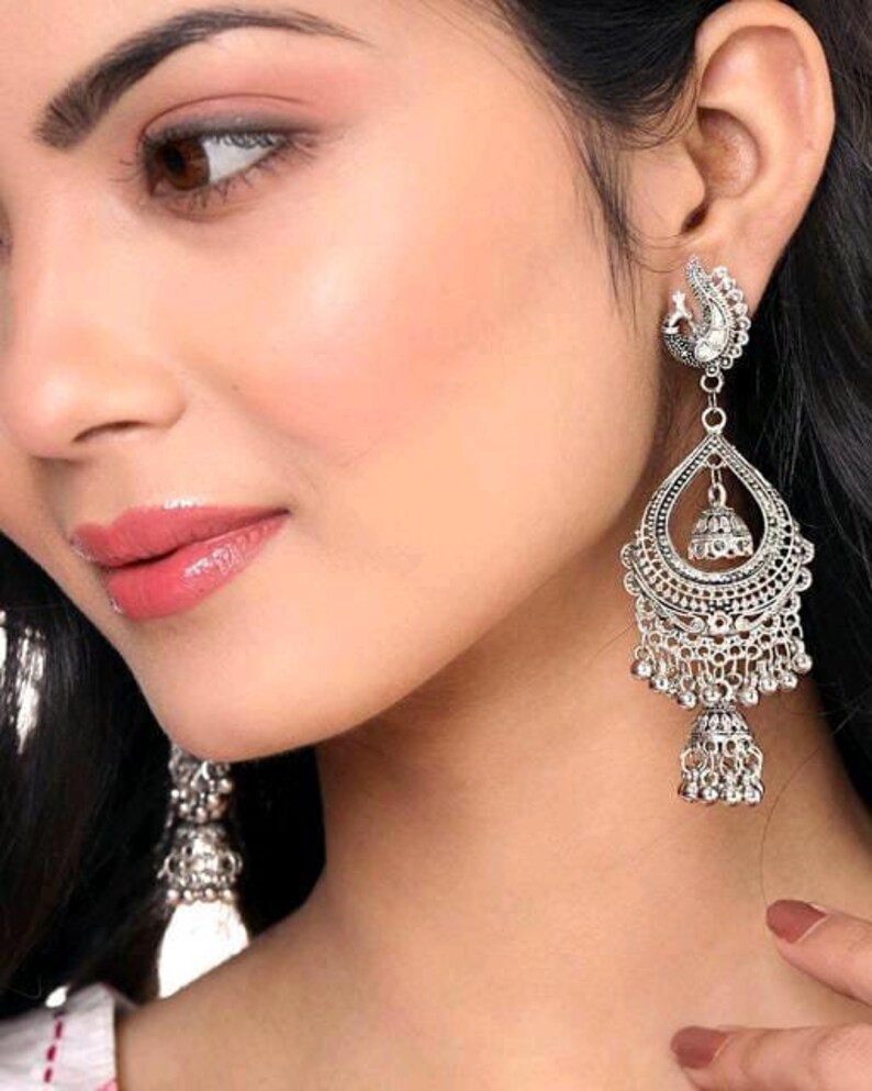 May include: Silver tone dangle earrings with a peacock design, a bell charm, and a beaded fringe.