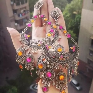May include: A pair of large silver earrings with pink and orange glass stones. The earrings have a crescent moon shape with intricate details and dangling charms.