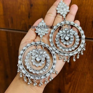 May include: Silver tone earrings with a circular design featuring multiple layers of clear stones. The earrings have a dangling design with small beads.