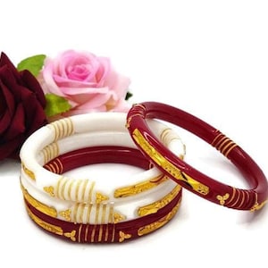 Op de afbeelding: Set van vier armbanden, twee wit en twee rood met gouden accenten. De armbanden zijn op elkaar gestapeld.