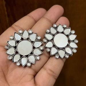 May include: A pair of silver tone earrings with a circular design. Each earring features a central mirror surrounded by smaller mirrored teardrop shapes.