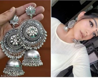 May include: A pair of silver dangle earrings with a floral design and a bell-shaped bottom. The earrings are made of metal and have a traditional Indian style.