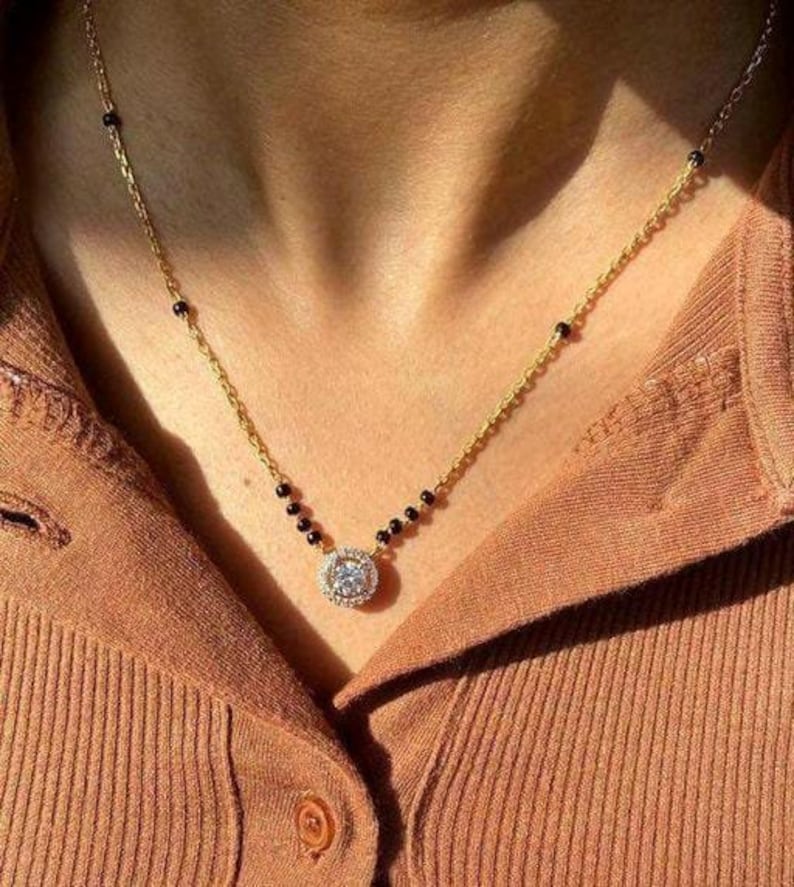 May include: A gold chain necklace with black beads and a round pendant featuring a large clear stone surrounded by smaller stones.