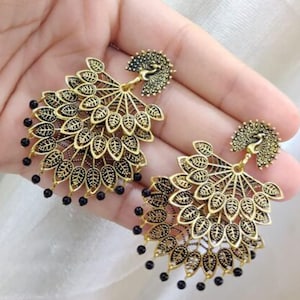 May include: Gold tone peacock earrings with black bead accents. The earrings feature a layered design with a peacock motif at the top.
