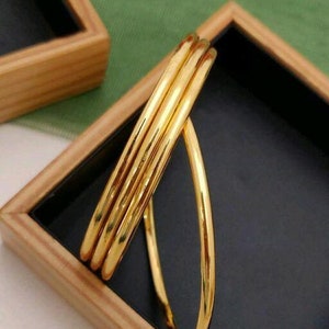 May include: Three gold bangles stacked on top of each other. The bangles are smooth and shiny.