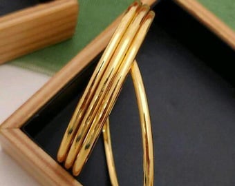 Könnte beinhalten: Drei goldene Armreifen, die übereinander gestapelt sind. Die Armreifen sind glatt und glänzend.