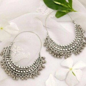 May include: A pair of silver hoop earrings with a beaded design and dangling charms. The earrings are on a white background.