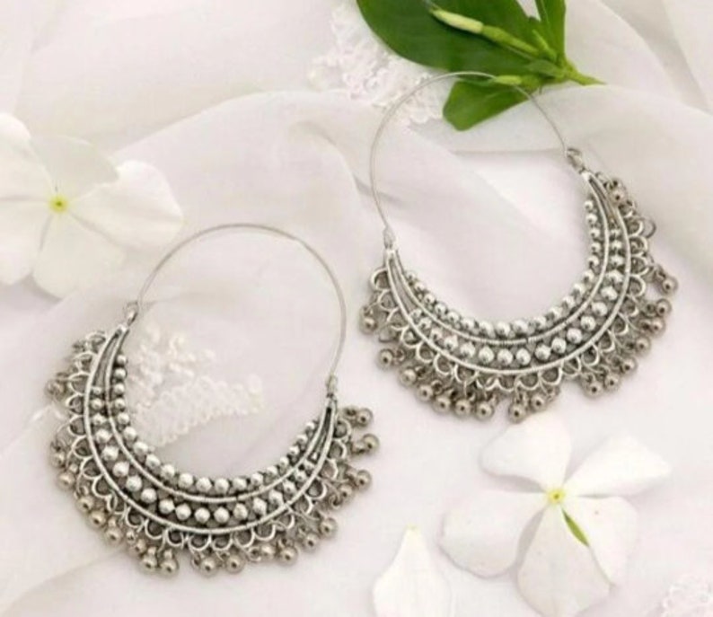 May include: A pair of silver hoop earrings with a beaded design and dangling charms. The earrings are on a white background.