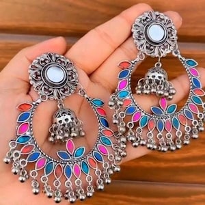 May include: Silver-coloured earrings with a floral design and colourful accents. The earrings feature a circular design with red, blue, and pink details, and small dangling beads. The earrings have a bell-shaped charm in the centre.
