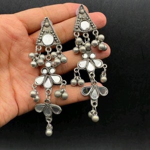 Puede incluir: Un par de pendientes de plata con múltiples detalles de espejo y pequeñas cuentas de plata. Los pendientes son de forma triangular y tienen un diseño colgante.
