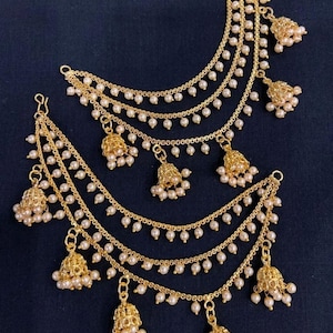 May include: A pair of gold-tone earrings with multiple strands of small white pearls and dangling bells. The bells are intricately designed and have a gold finish.