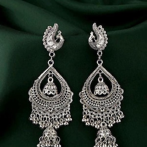 May include: Silver dangle earrings with a peacock design and multiple tiers of beads. The earrings have a silver bell at the bottom.