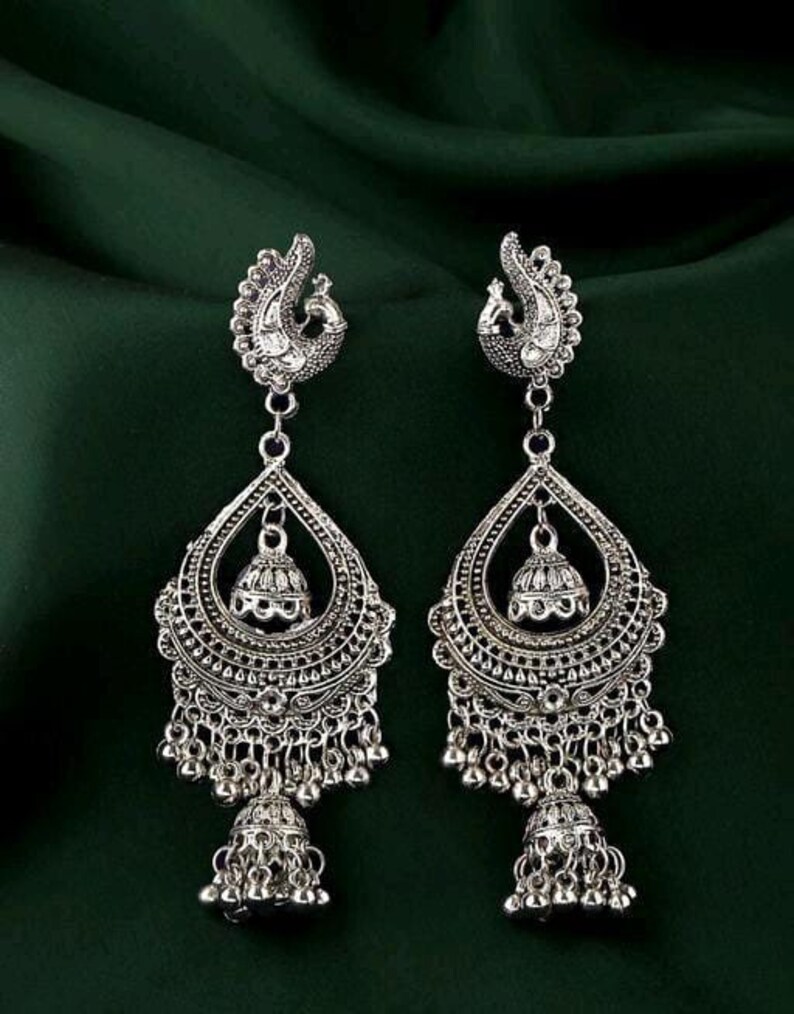 May include: Silver dangle earrings with a peacock design and multiple tiers of beads. The earrings have a silver bell at the bottom.