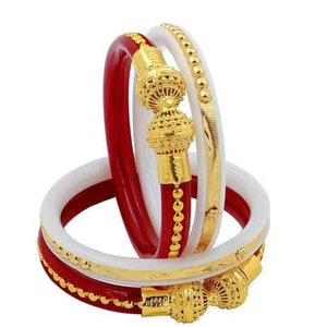 Könnte beinhalten: Set aus drei Armreifen, einer rot, einer weiß und einer mit goldenem Design. Die Armreifen sind übereinander gestapelt.
