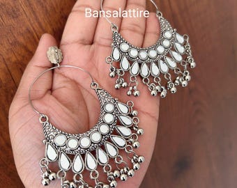 May include: A pair of silver hoop earrings with a crescent moon design. The earrings have a white mirror finish and dangle with small silver beads.