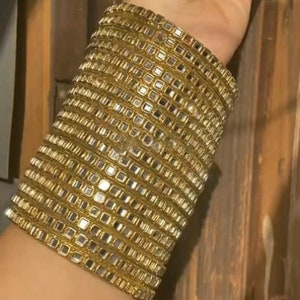 May include: A gold bangle bracelet with multiple layers of small, square, mirrored tiles.