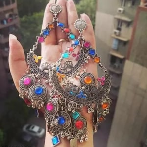 May include: A pair of silver earrings with colorful glass stones and intricate metalwork. The earrings feature a crescent moon shape with dangling charms and a long, beaded drop.