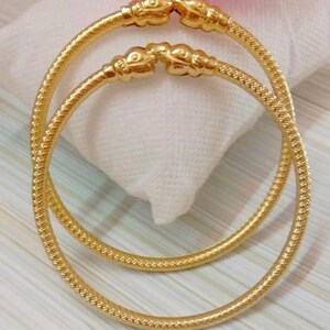 Peut inclure: Deux bracelets en or avec un motif texturé et des extrémités décoratives. Les bracelets sont empilés l'un sur l'autre.