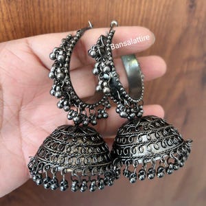 May include: A pair of silver oxidized earrings with a large, round, ornate design and a smaller, half-circle design with dangling beads.