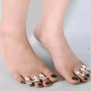 May include: A pair of silver toe rings with intricate floral designs. The rings are worn on the toes of a person's feet.