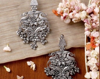 May include: A pair of silver earrings with a peacock and floral design. The earrings are intricate and detailed, with a dangling charm at the bottom.