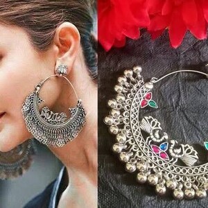 May include: Silver hoop earrings with a crescent moon design and dangling bells. The earrings have colorful stones and intricate details.