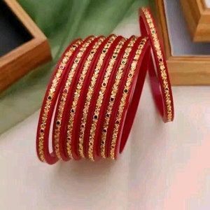 May include: A set of red bangles with gold and green accents. The bangles are stacked and arranged in a circular pattern.