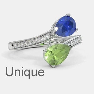 May include: A silver ring with a pear-shaped blue sapphire and a pear-shaped green peridot. The ring is set with small diamonds.
