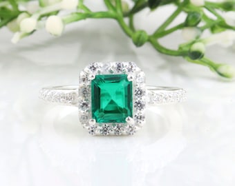 May include: A silver ring with a large emerald green square-shaped gemstone surrounded by a halo of smaller clear gemstones.