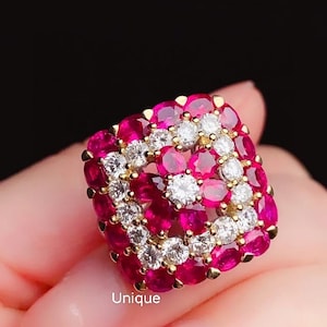 May include: A square-shaped ring with a gold band and a design of alternating red rubies and white diamonds.