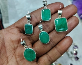 May include: Five emerald green gemstone pendants with silver settings. The pendants are displayed on a hand.
