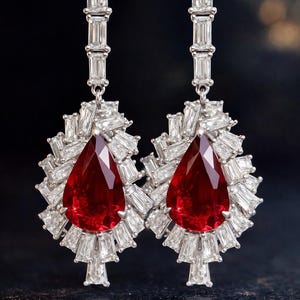 May include: A pair of elegant earrings featuring large, teardrop-shaped, deep red gemstones surrounded by a halo of smaller, rectangular, clear stones. The earrings have a linear design with multiple rectangular stones.