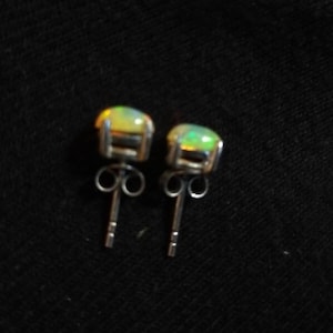 May include: A pair of silver stud earrings with oval-shaped opal gemstones. The opals are a pale yellow-green color with a slight iridescent shimmer.