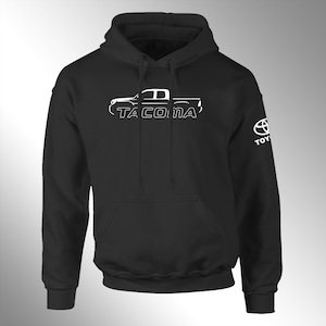 May include: Black hooded sweatshirt with a white outline of a Toyota Tacoma pickup truck and the word "TACOMA" printed on the front. The right sleeve has a white Toyota logo with the word "TOYOTA" printed below it.