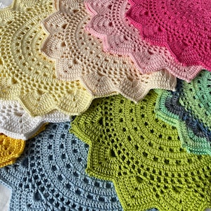 Può includere: Una collezione di tovagliette all'uncinetto in vari colori, tra cui bianco, giallo, azzurro, verde, rosa e grigio. Le tovagliette sono disposte a ventaglio, con la tovaglietta più grande in basso e la più piccola in alto.