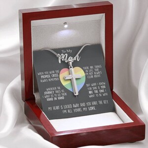Pu&ograve; includere: Una scatola di legno con il coperchio aperto, che rivela una collana d'argento con un ciondolo a forma di cuore arcobaleno e una croce. La collana &egrave; accompagnata da un biglietto con il testo "To My Man" e un messaggio sull'amore e l'impegno.