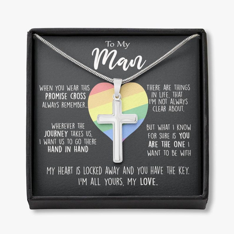 Pu&ograve; includere: Una collana d'argento con un ciondolo a forma di croce in una scatola nera. La scatola presenta un cuore arcobaleno con il testo "To My Man" e un messaggio su una croce di promessa e un viaggio fatto mano nella mano.