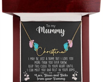 Puede incluir: Una caja de madera con un interior de terciopelo negro, que contiene un collar de oro con un dije de dos huellas de pies de bebé. El collar se presenta como un regalo para una madre con el mensaje "To my Mummy Christina, I may be just a bump, but I love you more than you ever know, keep this close to your heart until I can meet you and rest in your arms. Love, Kisses and Kicks from your Tummy."