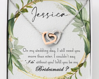 Peut inclure: Un collier argenté avec deux pendentifs en forme de cœur entrelacés, l'un en or rose et l'autre argenté, présenté dans un coffret cadeau. Le coffret porte le nom "Jessica" et le texte "Veux-tu être ma demoiselle d'honneur ?".