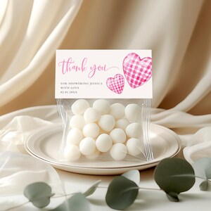 Könnte beinhalten: Ein klarer Zellophanbeutel gefüllt mit weißen Süßigkeiten, gekrönt von einer Karte mit der Aufschrift "thank you" in rosa Schrift. Die Karte zeigt zwei rosa Vichy-Herzen und den Text "For showering Jessica with love 02.01.20XX."