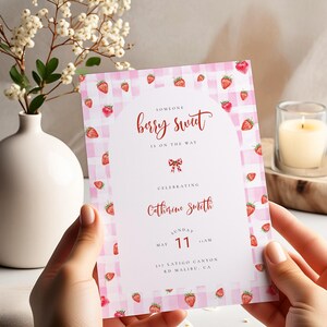 Könnte beinhalten: Eine rosa-weiß karierte Einladung mit Aquarell-Erdbeeren. Der Text lautet "Someone berry sweet is on the way" und feiert Catherine Smith. Das Datum ist der 11. Mai.