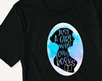 Può includere: Maglietta nera con una silhouette di una testa di donna e il testo "Just a girl who loves books" in un ovale acquerellato blu e viola.