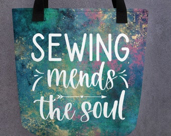 May include: A teal and gold tote bag with a white graphic that says "Sewing mends the soul" with an arrow pointing to the word "soul".